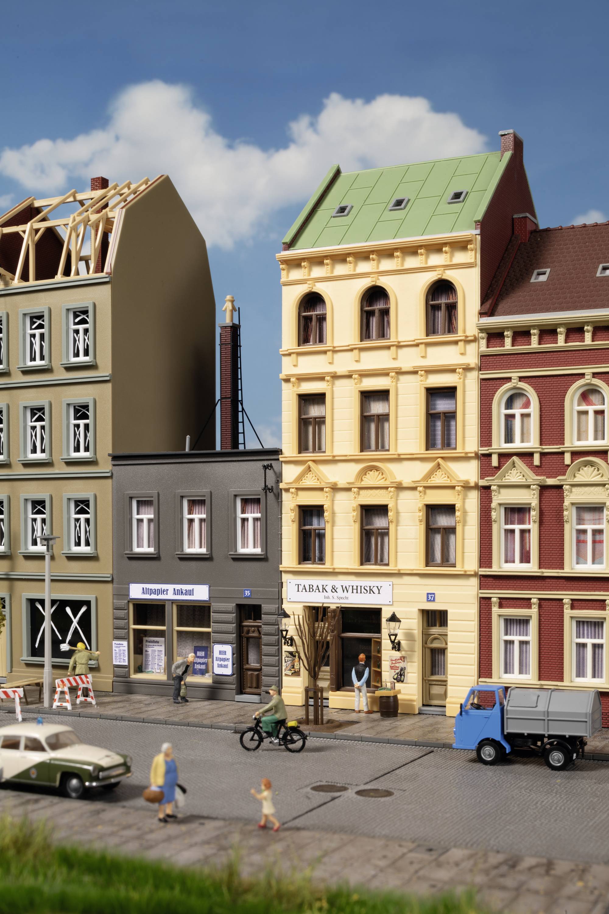 Modell einer Straßenszene mit drei Stadthäusern, einem Lastwagen, einem Motorrad und Fußgängern. Ein Schild zeigt 'TABAK & WHISKY'.