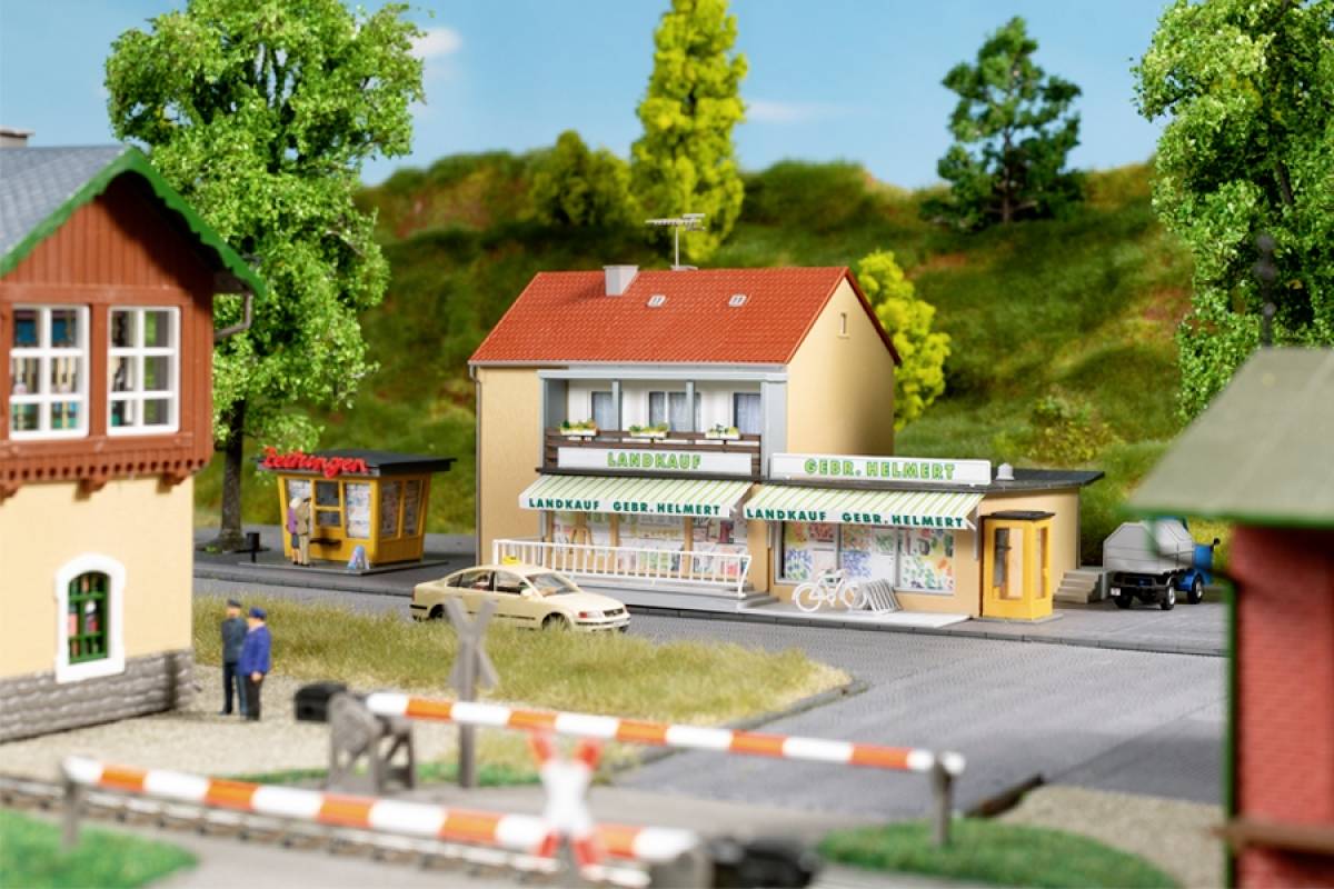 Miniaturmodell einer Stadt mit Gebäuden und Figuren. Ein Gebäude trägt das Schild 'Landarzt' und 'GEO HELMERT'. Im Vordergrund sind Schranken.