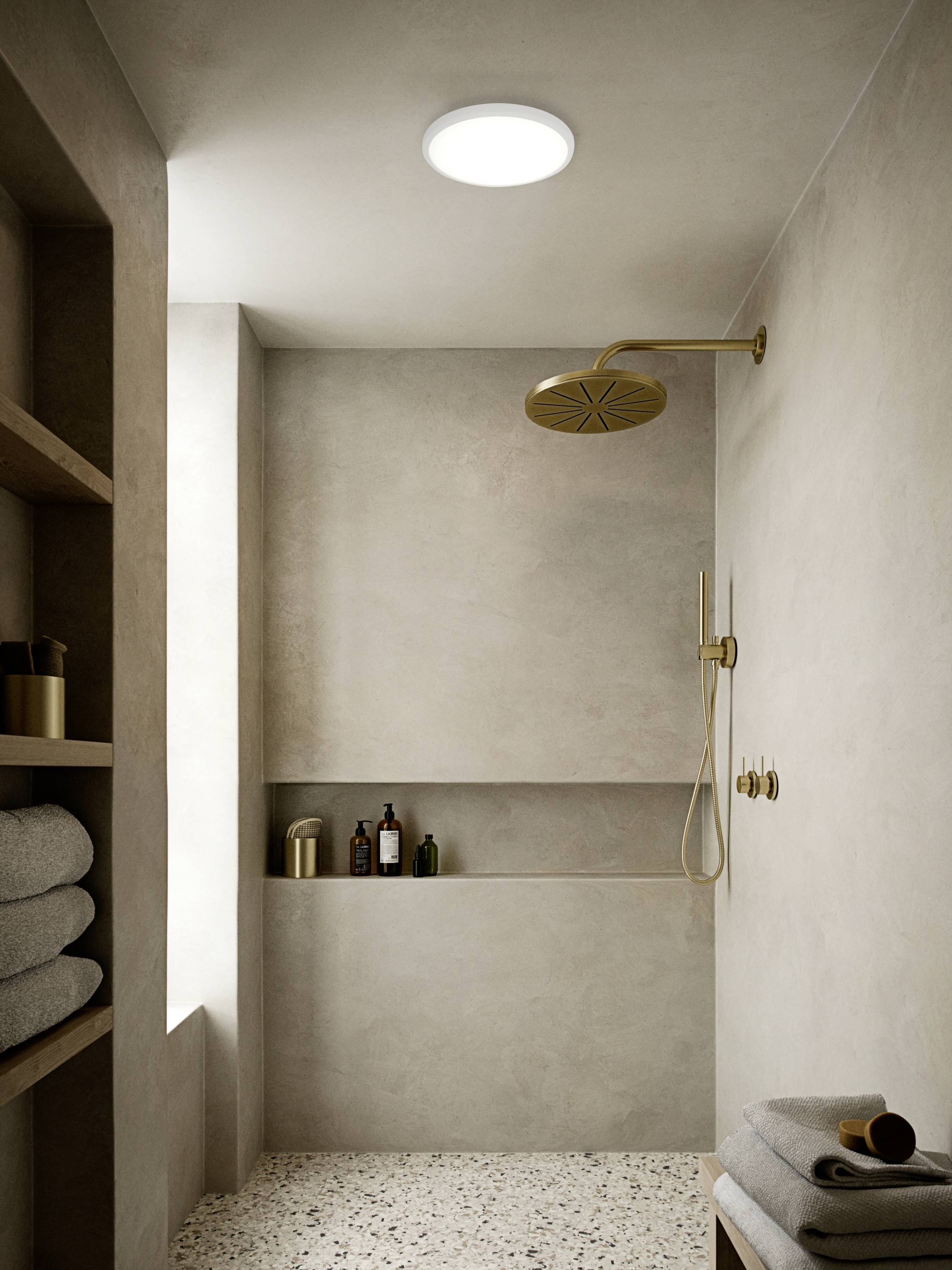 Ein modernes Badezimmer mit einer offenen Dusche. Die hellen Wände und der runde Duschkopf schaffen eine minimalistische Atmosphäre. Im Regal liegen Handtücher.