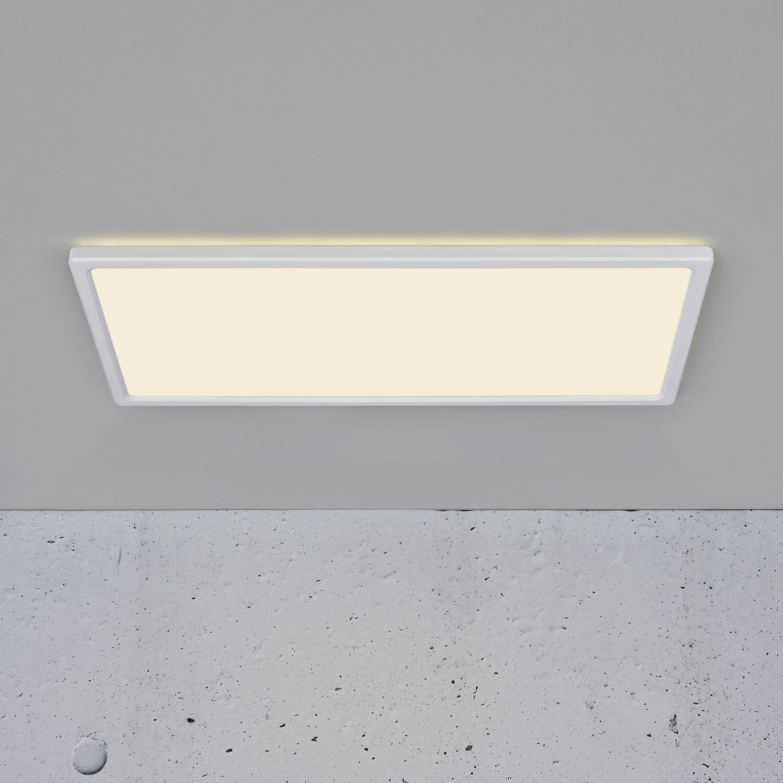 Rechteckige LED-Deckenleuchte leuchtet in einem schlichten, grauen Raum.