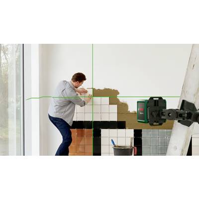 Ein Mann bringt Fliesen an einer Wand an, während ein Laser-Nivelliergerät grüne Linien zur Unterstützung projiziert.