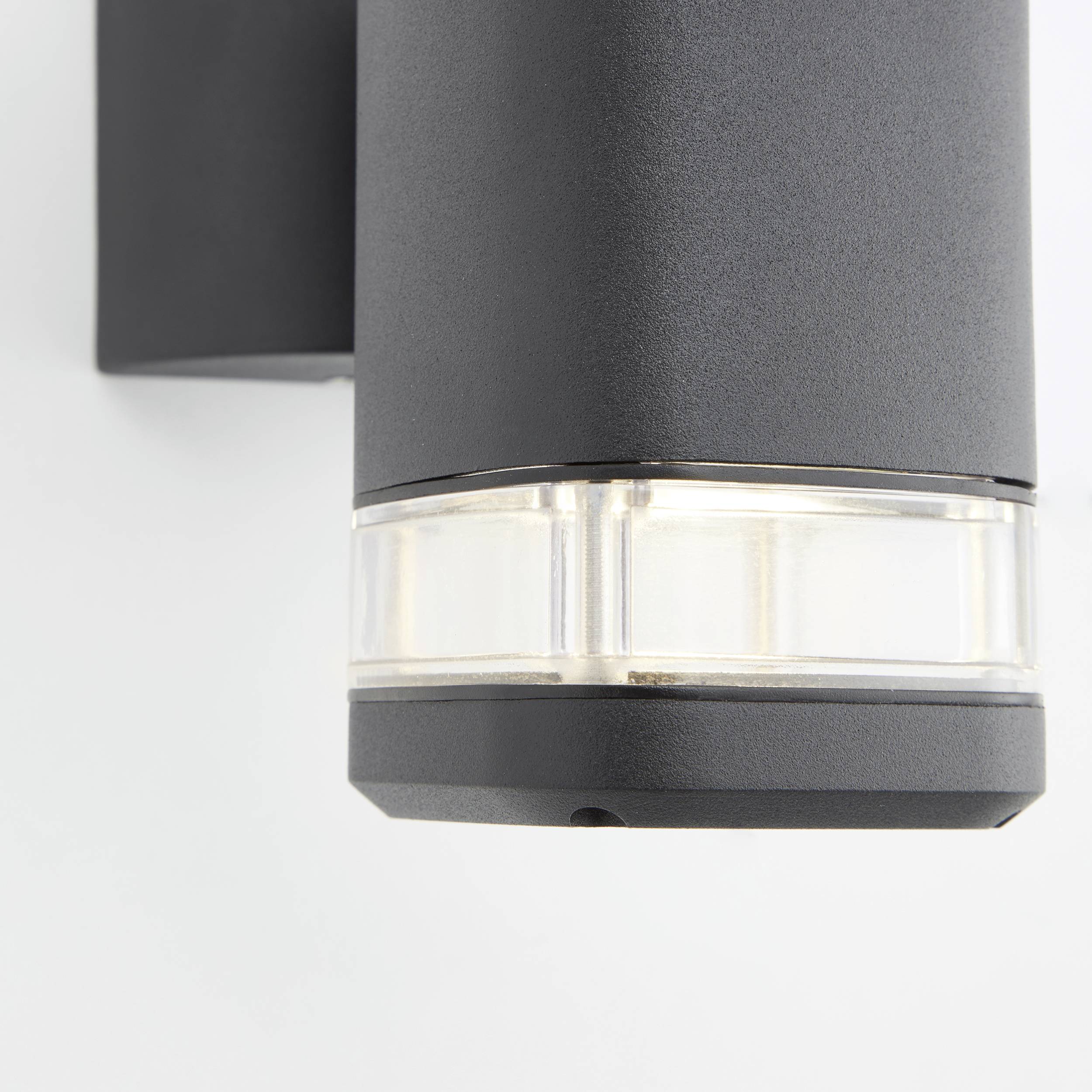Schwarze, moderne Außenwandlampe mit zylindrischem Design und transparentem Abschnitt für Lichtaustritt, in Nahaufnahme gezeigt.