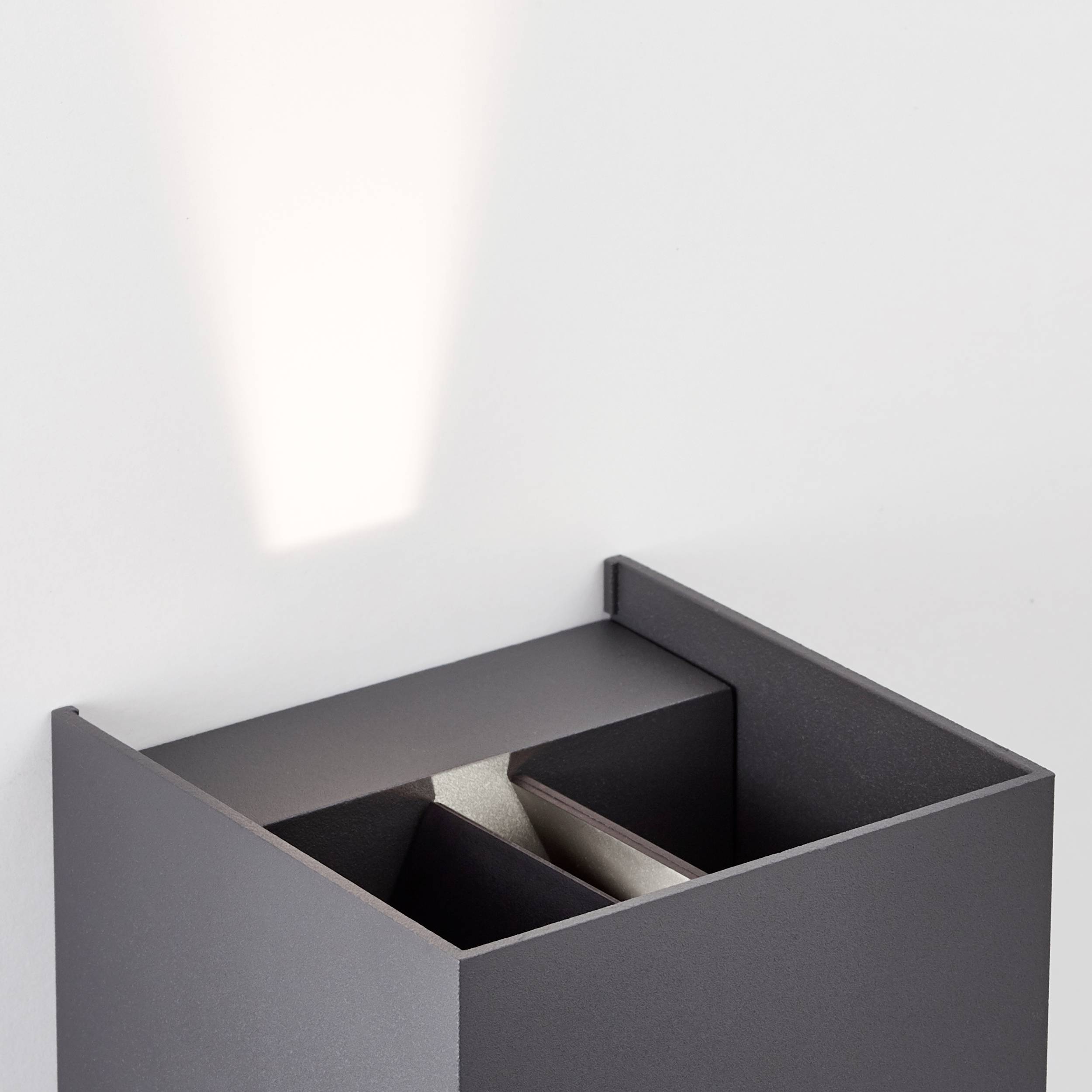Wandlampe in modernem Design, wirft einen schräg nach oben gerichteten Lichtstrahl an die Wand. Minimalistischer Stil in Grau.