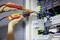 Eine Person misst mit einem elektrischen Prüfgerät die Spannung in einem Schaltschrank mit zahlreichen Kabeln und Schaltungen.