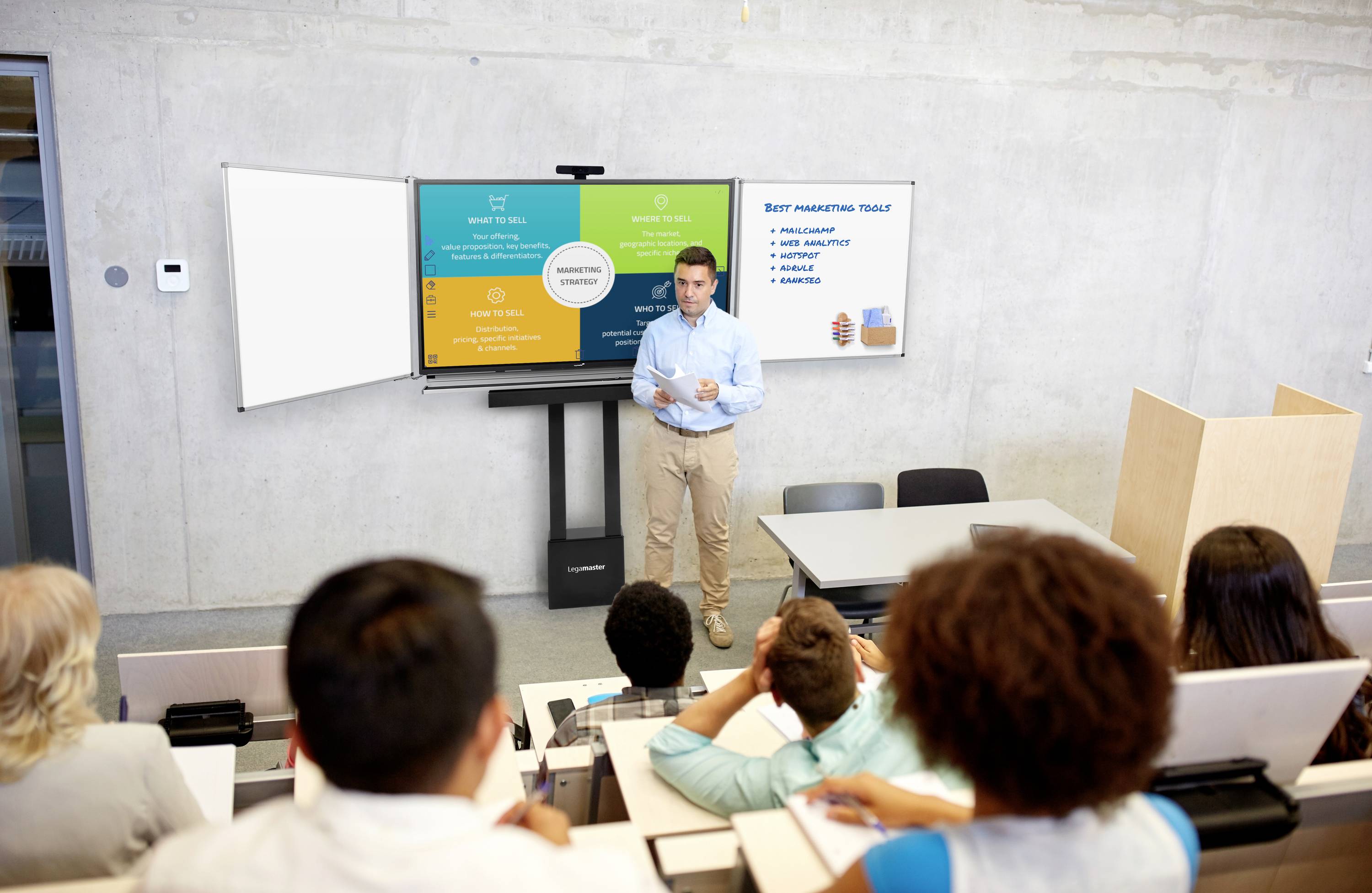 Ein Mann präsentiert in einem Seminarraum vor einer Leinwand, auf der farbcodierte Informationen zum Thema 'Best Marketing Tools' angezeigt werden.