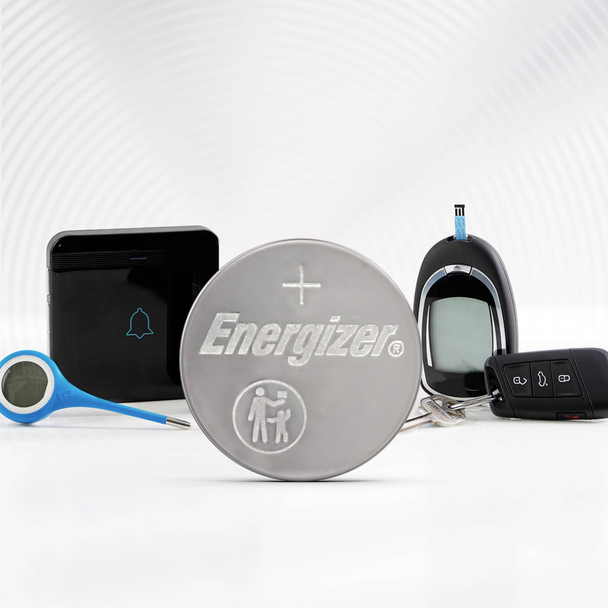 Eine Energizer-Knopfzelle liegt im Vordergrund, umgeben von elektronischen Geräten und einem Autoschlüssel.
