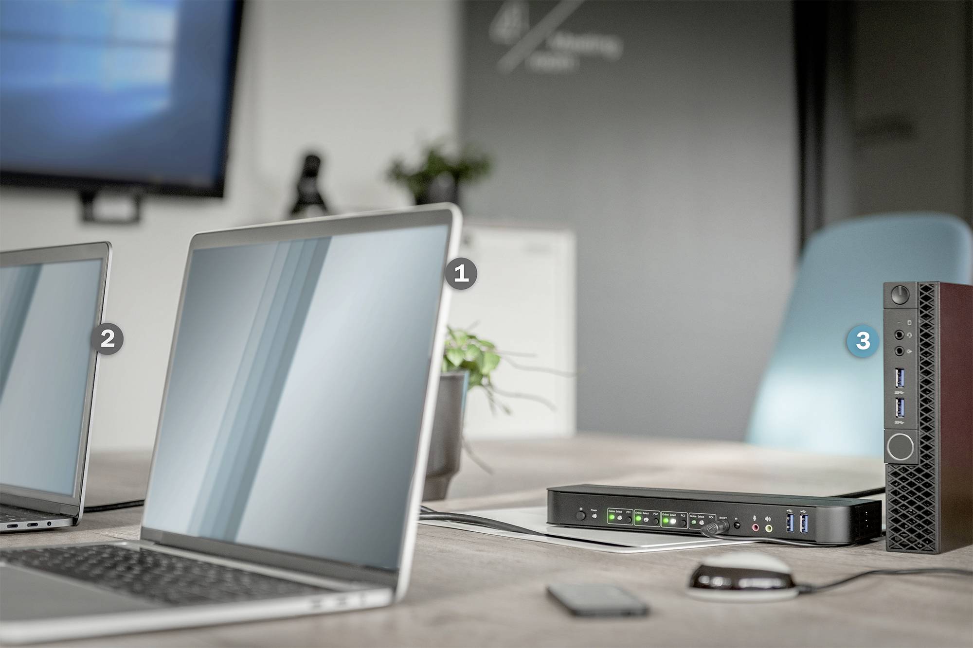 Ein Besprechungsraum mit zwei Laptops auf einem Tisch, verbunden mit einem Docking-Station und einem kleinen Gerät daneben.