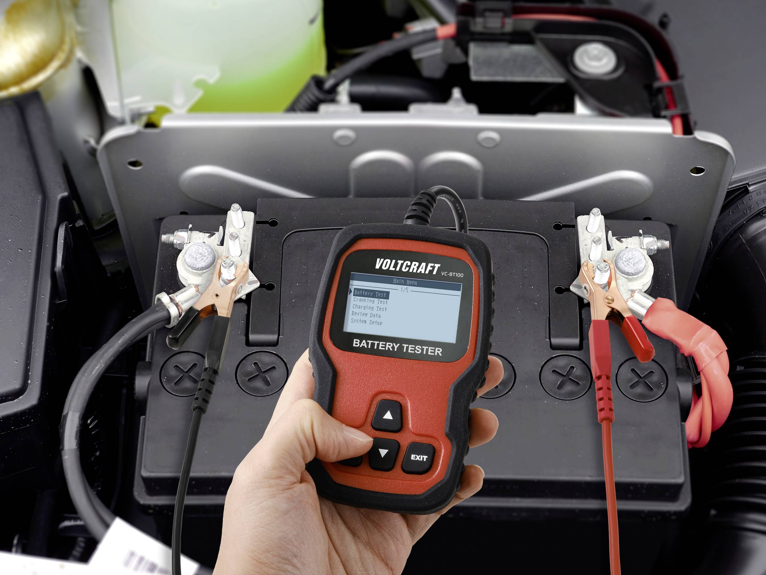 Eine Hand hält einen Batterietester, der an eine Autobatterie angeschlossen ist. Der Bildschirm zeigt Testergebnisse an.