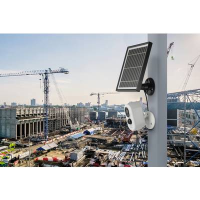 Überwachungs- und Solaranlage auf Mast vor großem Baustellengelände mit Kränen und Gebäudestruktur im Hintergrund.