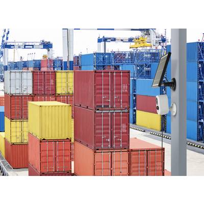 Containerhafen mit gestapelten bunten Frachtcontainern und einem Überwachungssystem im Vordergrund. Kräne im Hintergrund.