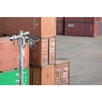 Eine Überwachungskamera mit Solarmodul überwacht einen Lagerplatz mit gestapelten Frachtcontainern im Hintergrund.