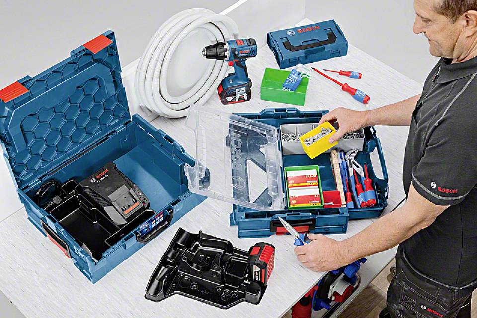 Ein Mann öffnet mehrere Werkzeugkoffer mit Elektrowerkzeugen und Zubehör, darunter eine Bohrmaschine, Akkulader und Kabel.