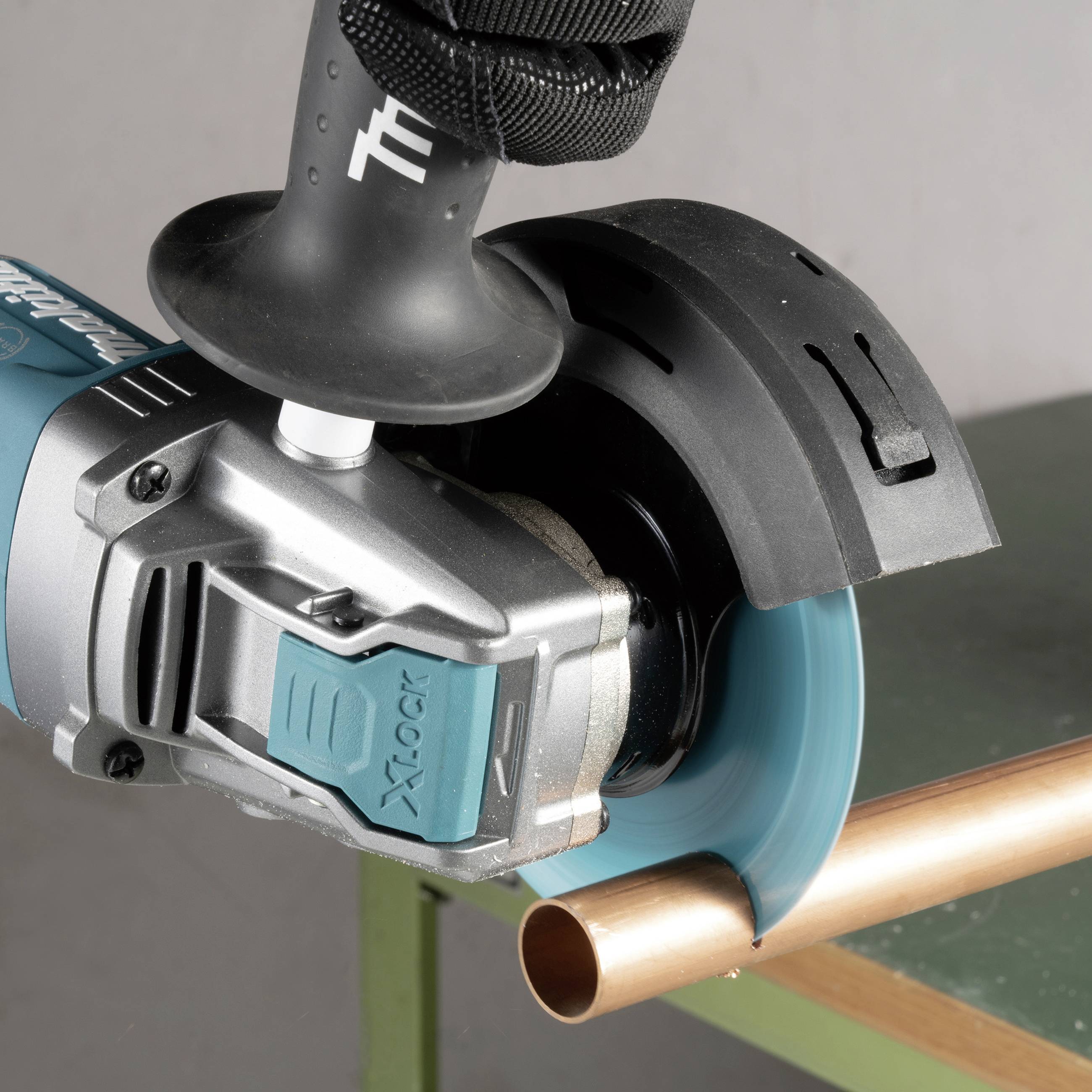 Eine elektrische Winkelschleifmaschine schneidet ein Kupferrohr auf einem grünen Tisch. Das Werkzeug hat eine blaue Schutzabdeckung.