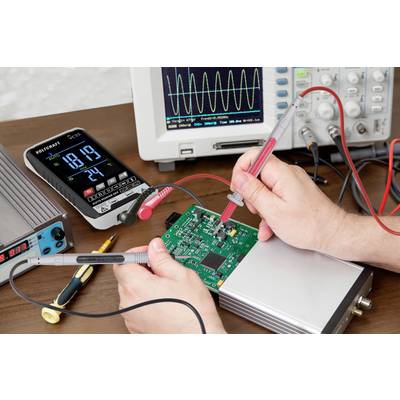 'Instandsetzung eines elektronischen Geräts': Eine Person benutzt Messgeräte, um eine grüne Schaltplatte zu testen. Oszilloskop im Hintergrund.