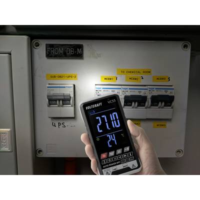 Eine Hand hält ein digitales Voltmeter vor einem Sicherungskasten. Der Bildschirm zeigt 271,0 Volt und 24 Grad Celsius an.