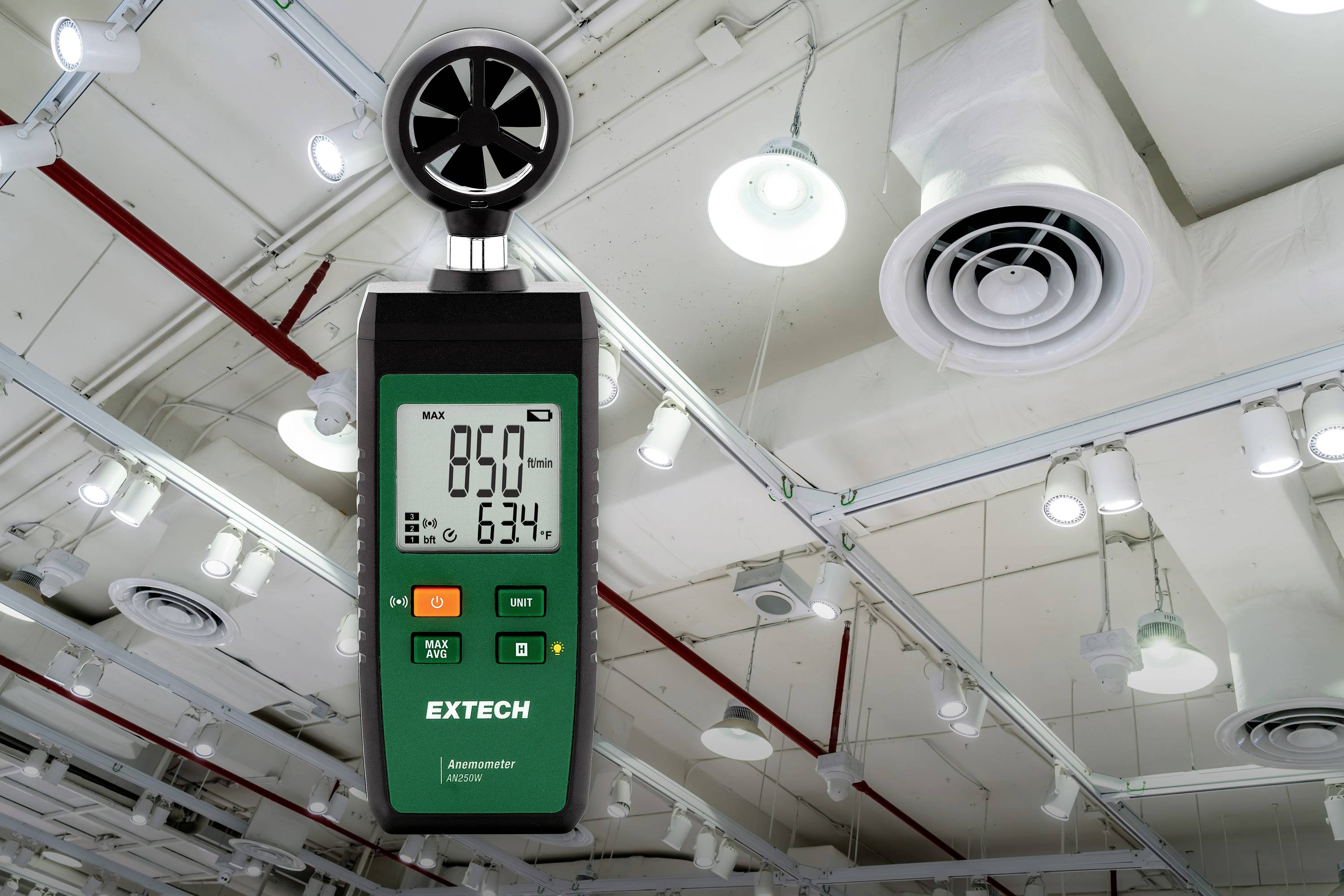 Ein Anemometer misst die Windgeschwindigkeit in einem großen Raum mit Deckenlüftern und Beleuchtung. Das Display zeigt '850' und '634' an.