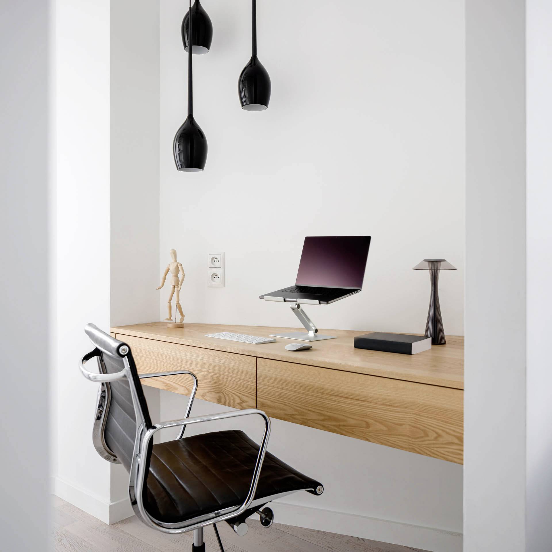 Ein minimalistisches Homeoffice mit einem Holzschreibtisch, schwarzem Stuhl, einem Laptop auf einem Ständer und modernen Lampen.