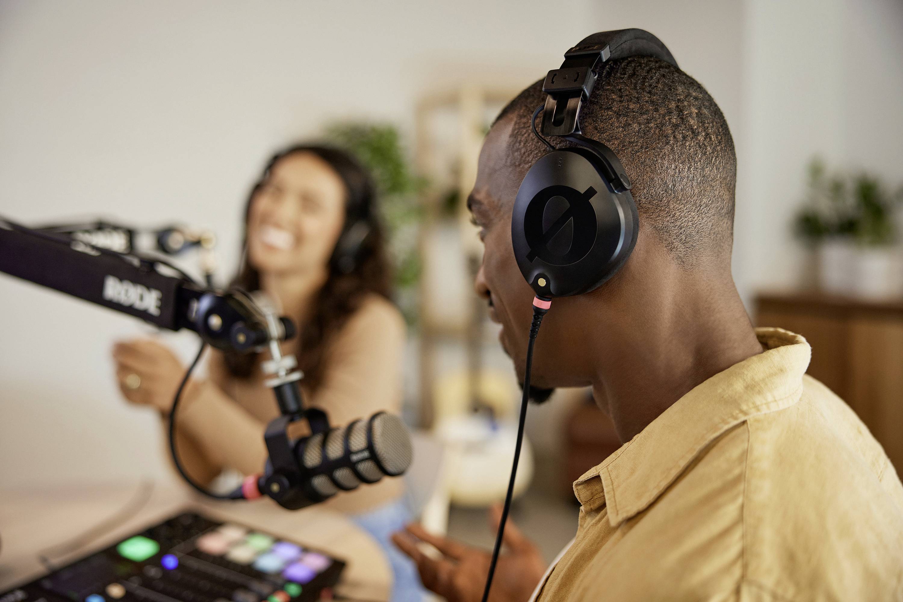 Zwei Personen nehmen in einem modernen Studio einen Podcast auf. Der Vordergrund zeigt einen Mann mit Kopfhörern und Mikrofon.
