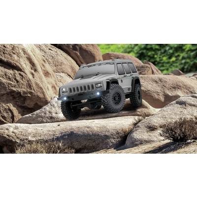 Ein grau-silberner Geländewagen fährt über große Felsen in einer felsigen Landschaft, umgeben von spärlicher Vegetation.
