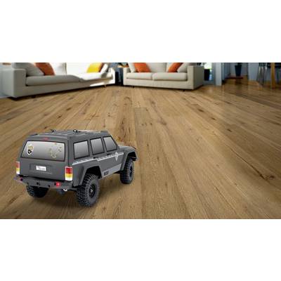 Ein Spielzeugauto im SUV-Stil auf einem Holzboden in einem Wohnzimmer mit beigen Sofas und orangefarbenen Kissen im Hintergrund.