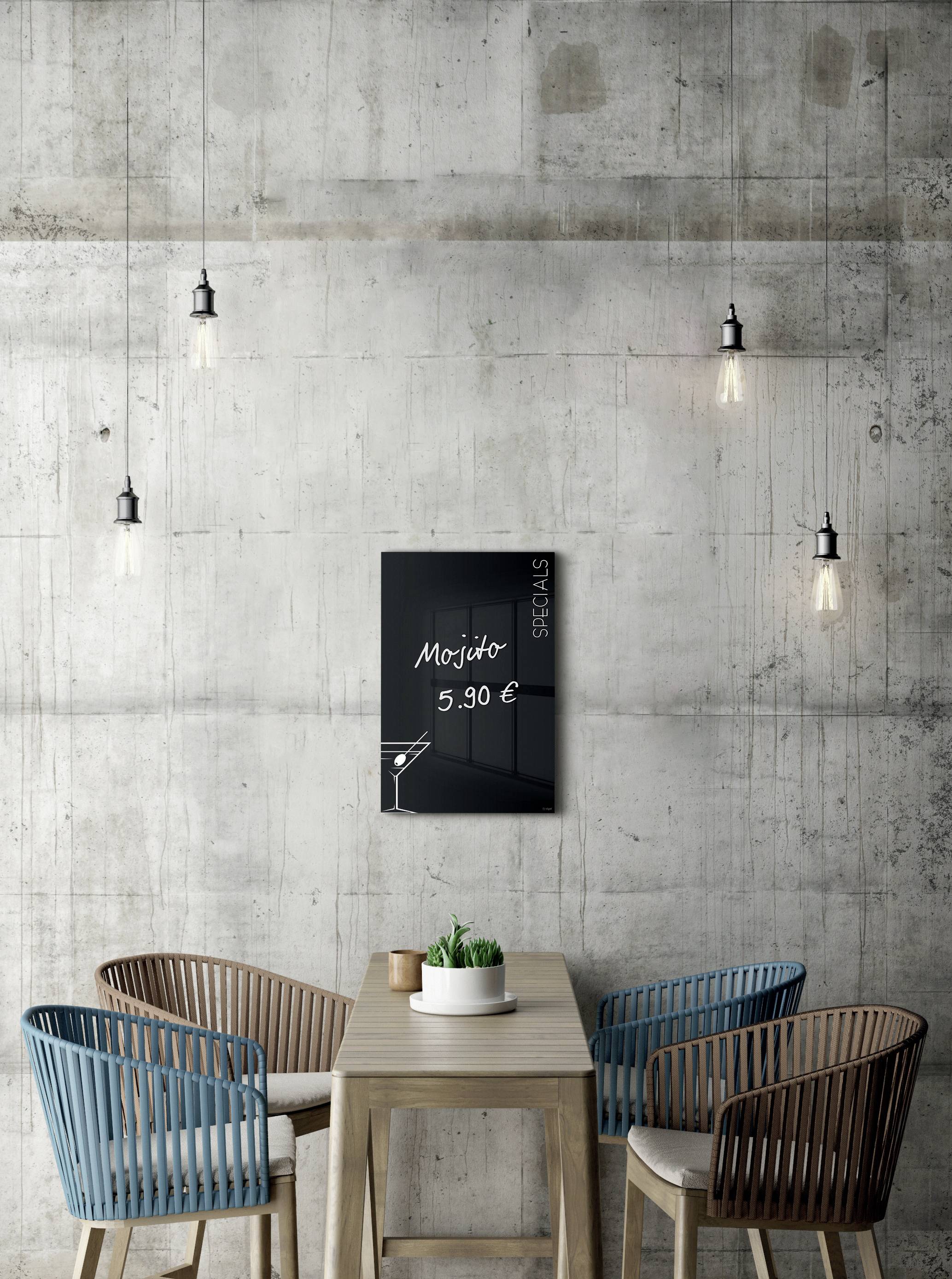 Ein Tisch mit vier Stühlen steht unter einer Tafel, die 'Mojito 5,90 EUR' anzeigt. Hängelampen erleuchten den Betonhintergrund.