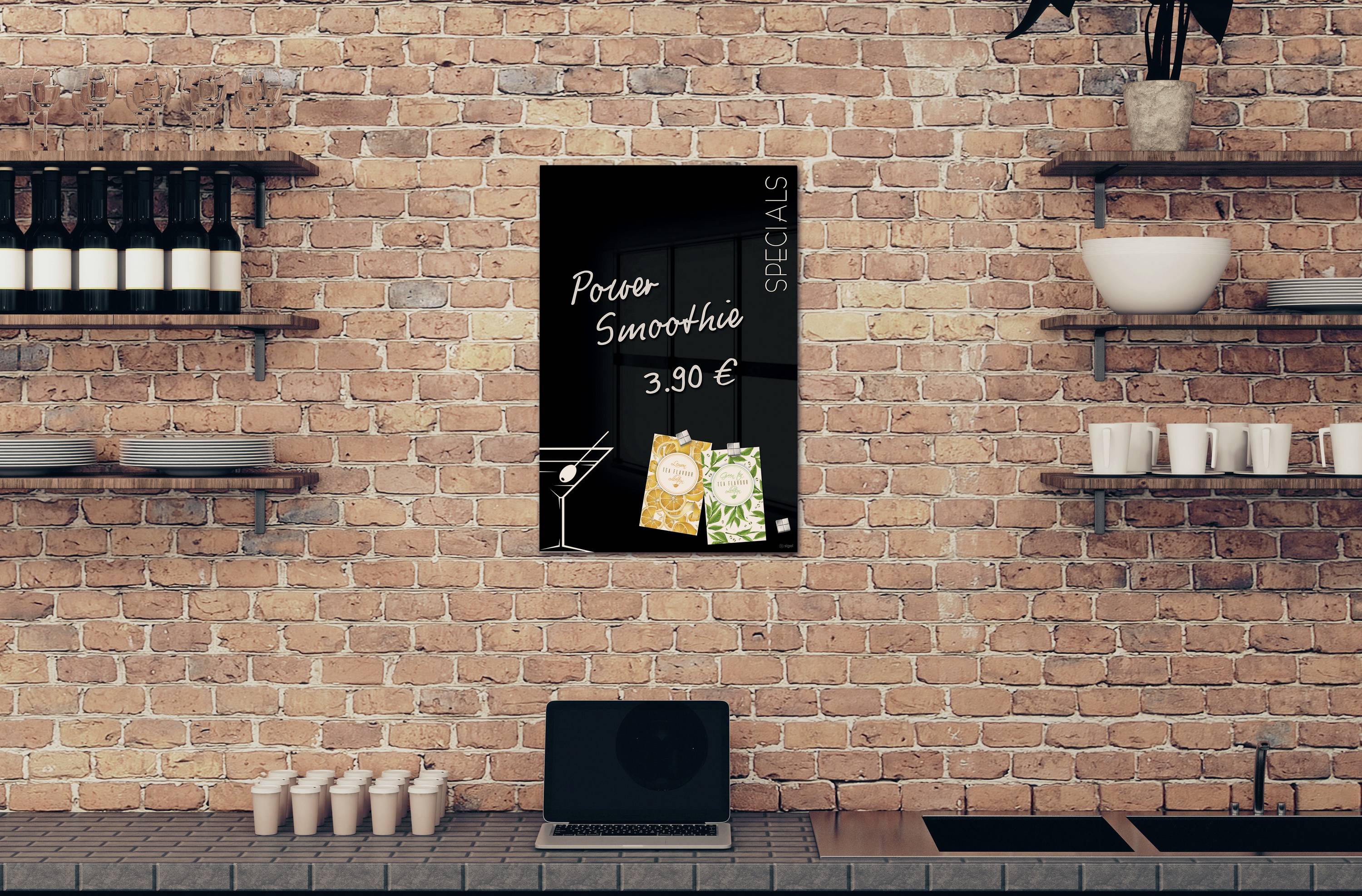 An einer Ziegelwand hängt ein Schild mit 'Poire Smoothie 3,90 EUR'. Daneben sind zwei Smoothie-Tüten abgebildet. Unter dem Schild stehen Regale mit Flaschen und ein Laptop.