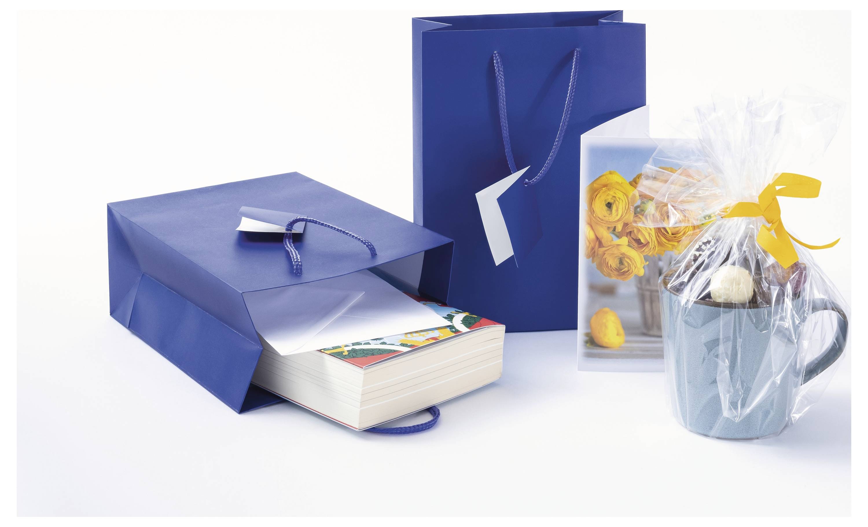 Blaue Geschenktüten und eine umwickelte Tasse mit Blumenmotiven, zeigen sortierte Geschenkverpackungen und Geschenke auf weißem Hintergrund.