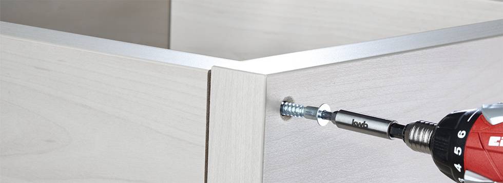 Eine elektrische Bohrmaschine zieht eine Schraube in ein Holzmöbelstück ein, zeigt den Aufbau oder die Reparatur des Möbelstücks.
