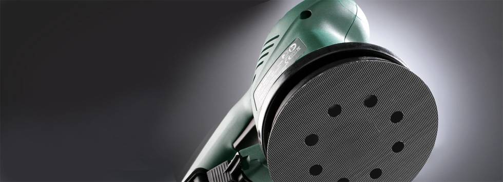 Grüner Exzenterschleifer in Nahaufnahme, zeigt die runde Schleiffläche mit mehreren Löchern, rechter Bildrand unscharf.