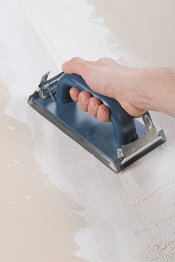 'Hand schleift eine verputzte Wand mit einem Schleifblock ab, um die Oberfläche zu glätten.'