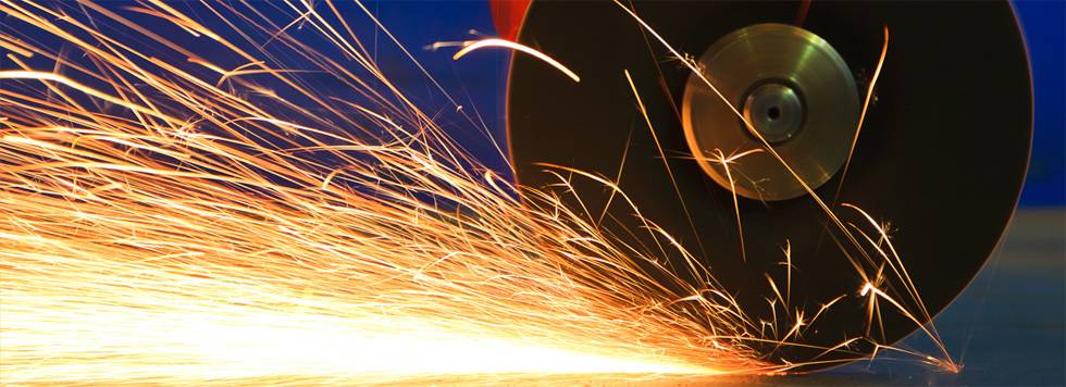 Ein Funkenregen entsteht beim Schleifen eines metallischen Werkstücks mit einer schnell rotierenden Scheibe.