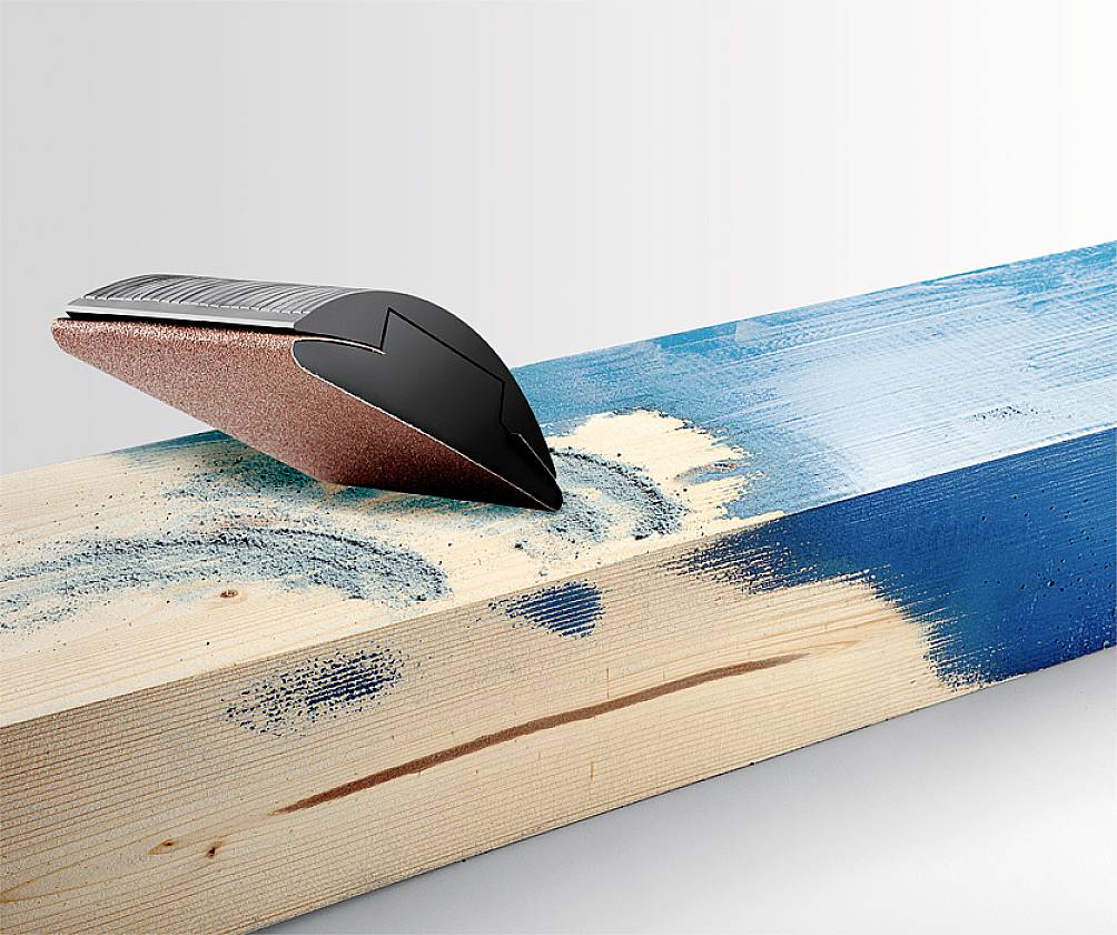 Holzschleifblock entfernt blaue Farbe von einem Holzstück. Das Bild zeigt den Fortschritt des Schleifens an einem farbigen Balken.