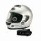 Ein silberner Motorradhelm mit eingebautem Mikrofon und Lautsprechern, verbunden mit einem externen Kommunikationsgerät, Markenlogo sichtbar.