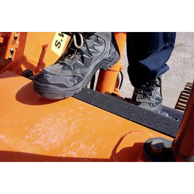 Ein Arbeiter steht mit robusten Wanderschuhen auf einer orangefarbenen Plattform einer schweren Baumaschine.