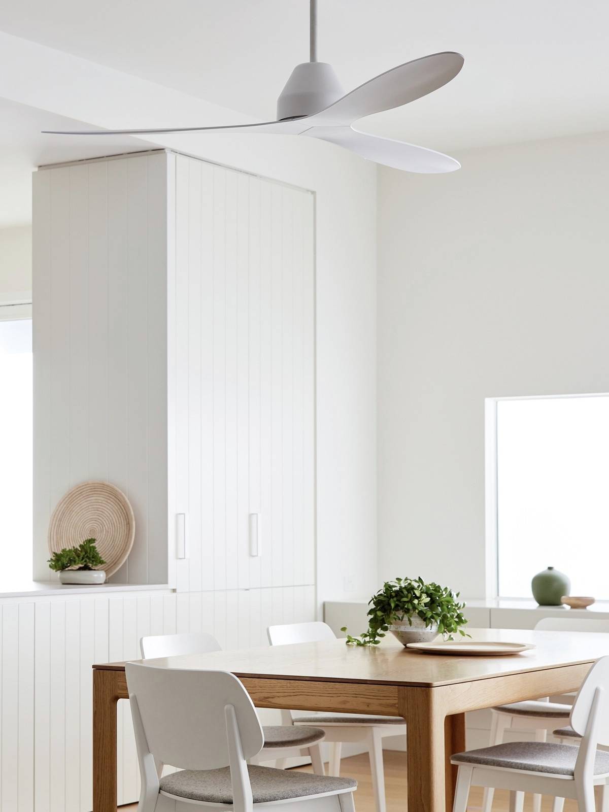 Moderner Essbereich mit Holztisch, vier weißen Stühlen und einem Deckenventilator. Fenster lässt Tageslicht herein, Pflanzen als Dekoration.