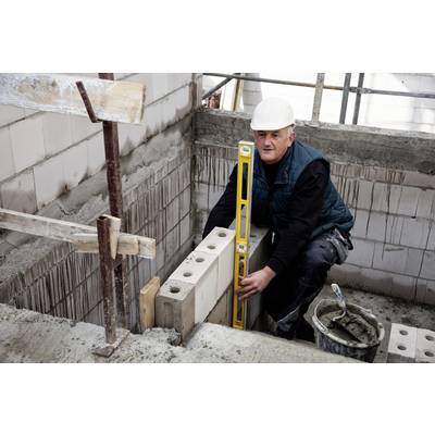 Ein Bauarbeiter mit Schutzhelm verwendet eine Wasserwaage, um die Ausrichtung von Ziegeln in einer Mauer auf einer Baustelle zu überprüfen.