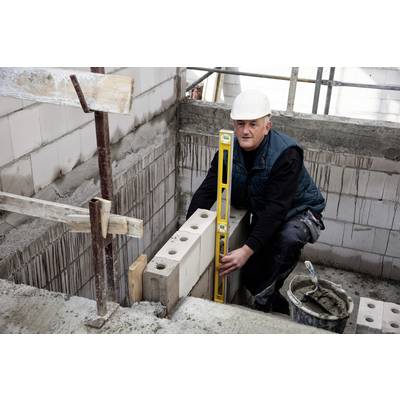 Ein Bauarbeiter mit Helm überprüft mit einer Wasserwaage die Ausrichtung von Backsteinen an einer Mauer auf einer Baustelle.