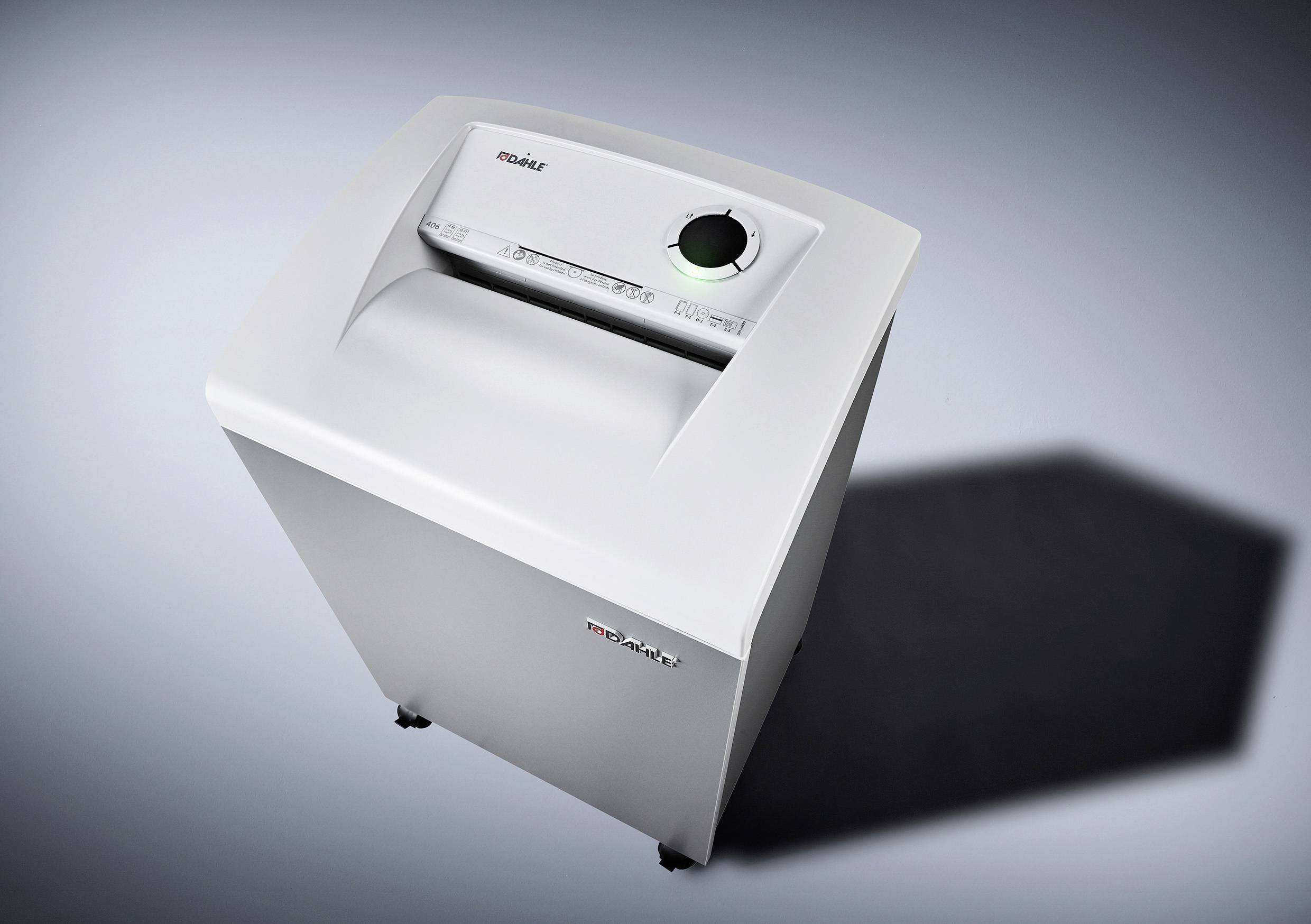 Ein moderner Aktenvernichter auf einem grauen Boden, schräg von oben fotografiert. Das Design ist kompakt und in neutralen Farben gehalten.