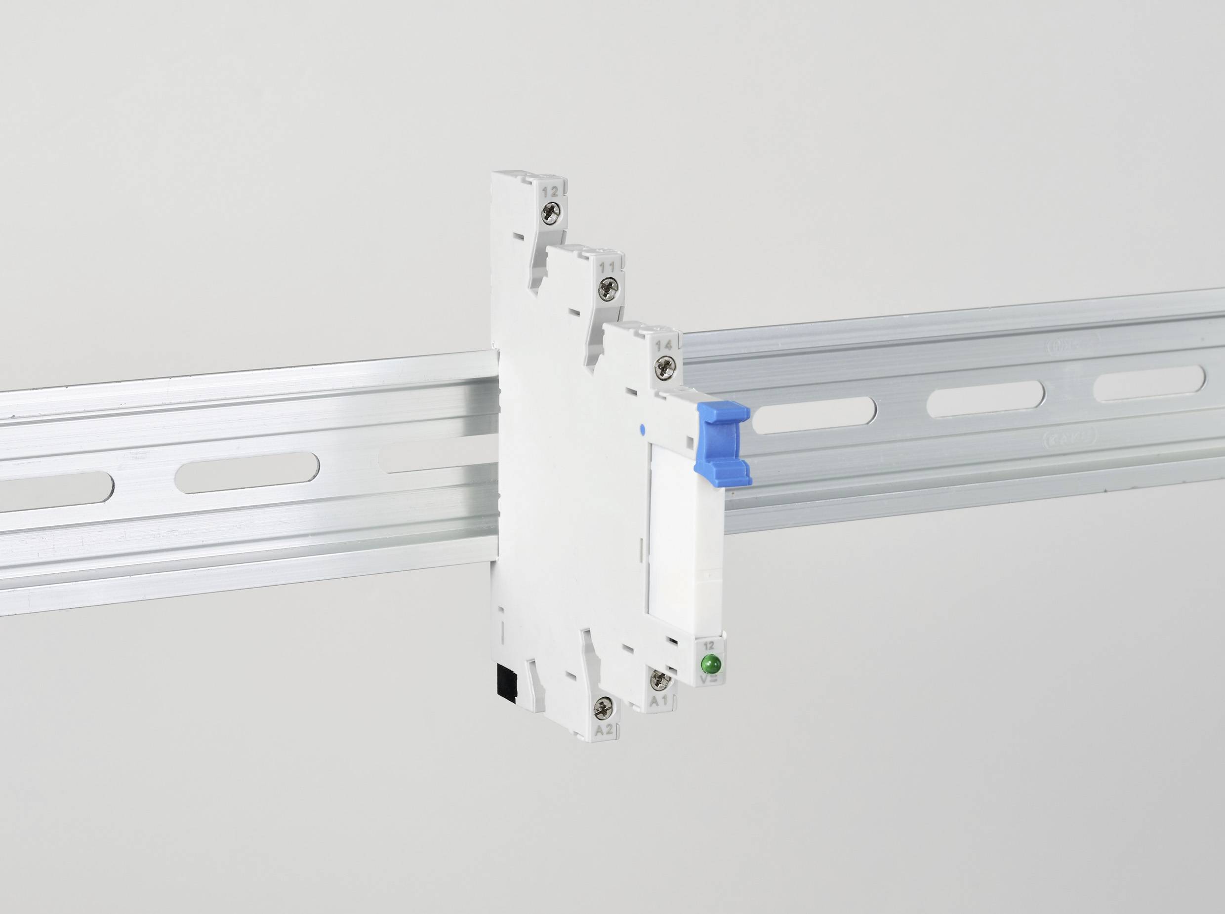 Ein weißer elektrischer Schalter mit blauer Betätigung auf einer Metall-Hutschiene, vor hellem Hintergrund montiert.