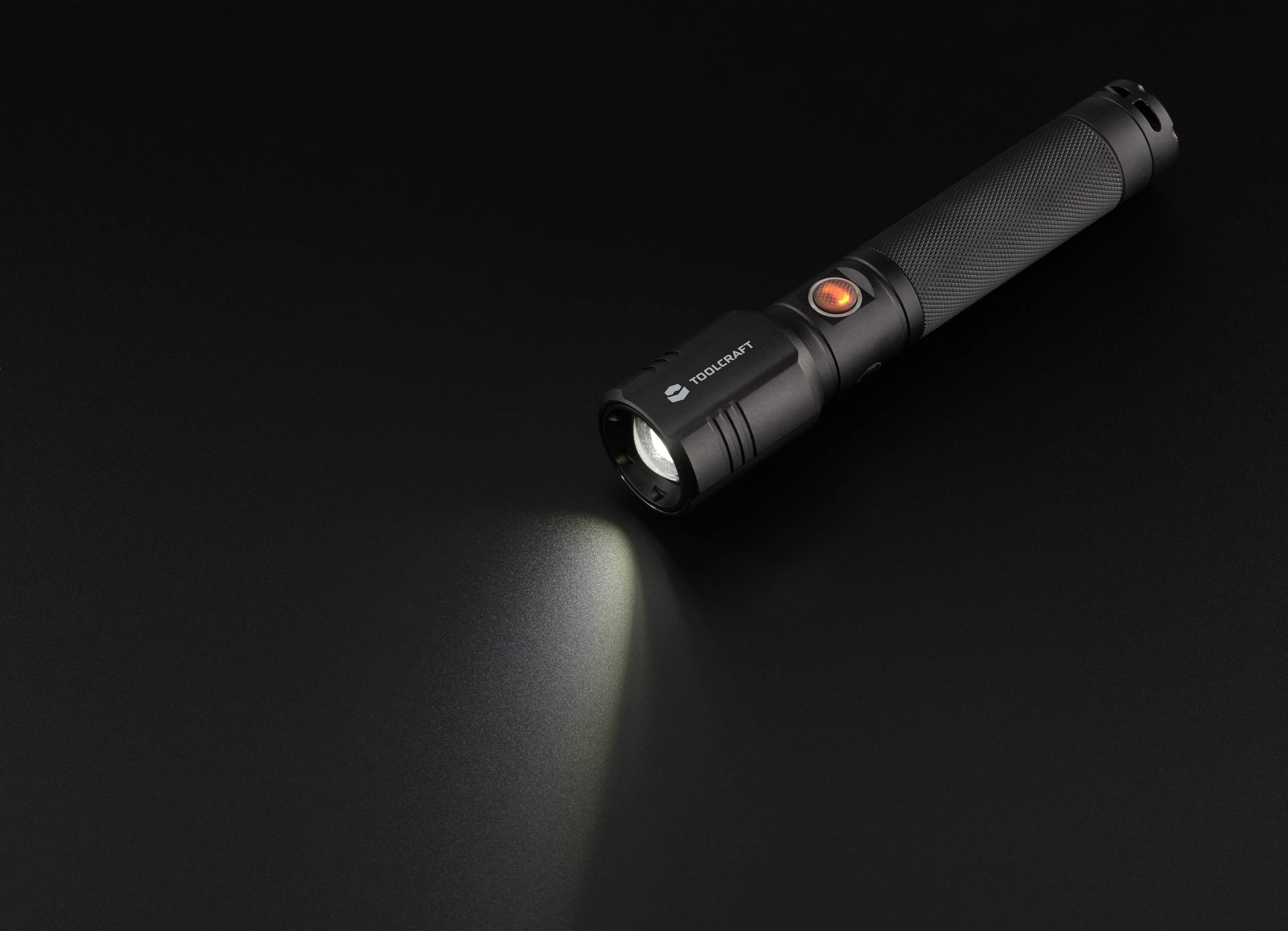 Schwarze Taschenlampe auf dunklem Hintergrund, leuchtet nach links. Modell mit orangenem Schalter.