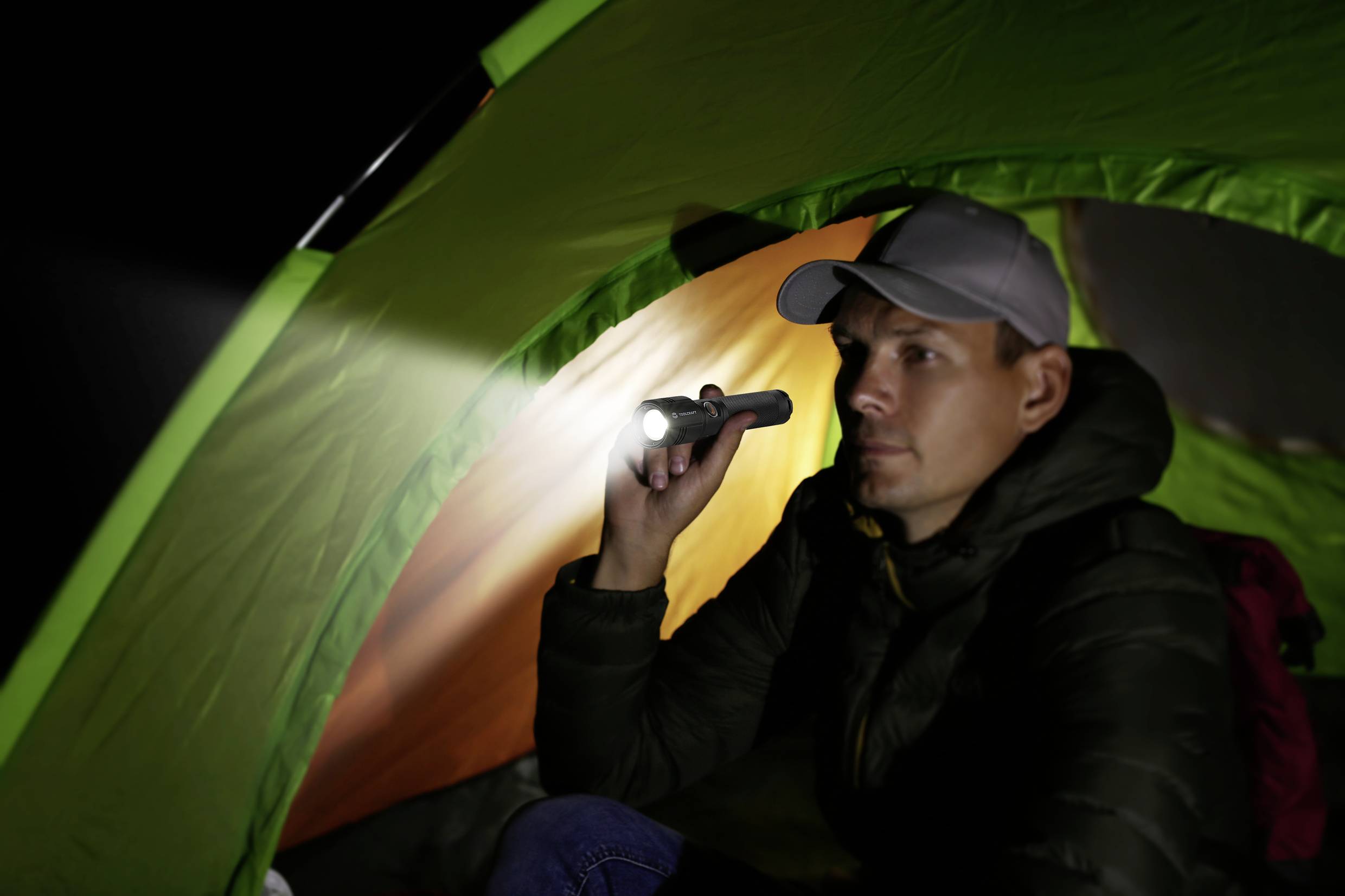 Ein Mann sitzt im Dunkeln in einem grünen Zelt und hält eine leuchtende Taschenlampe.