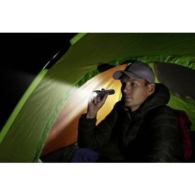 Ein Mann sitzt im Dunkeln in einem grünen Zelt und hält eine leuchtende Taschenlampe.