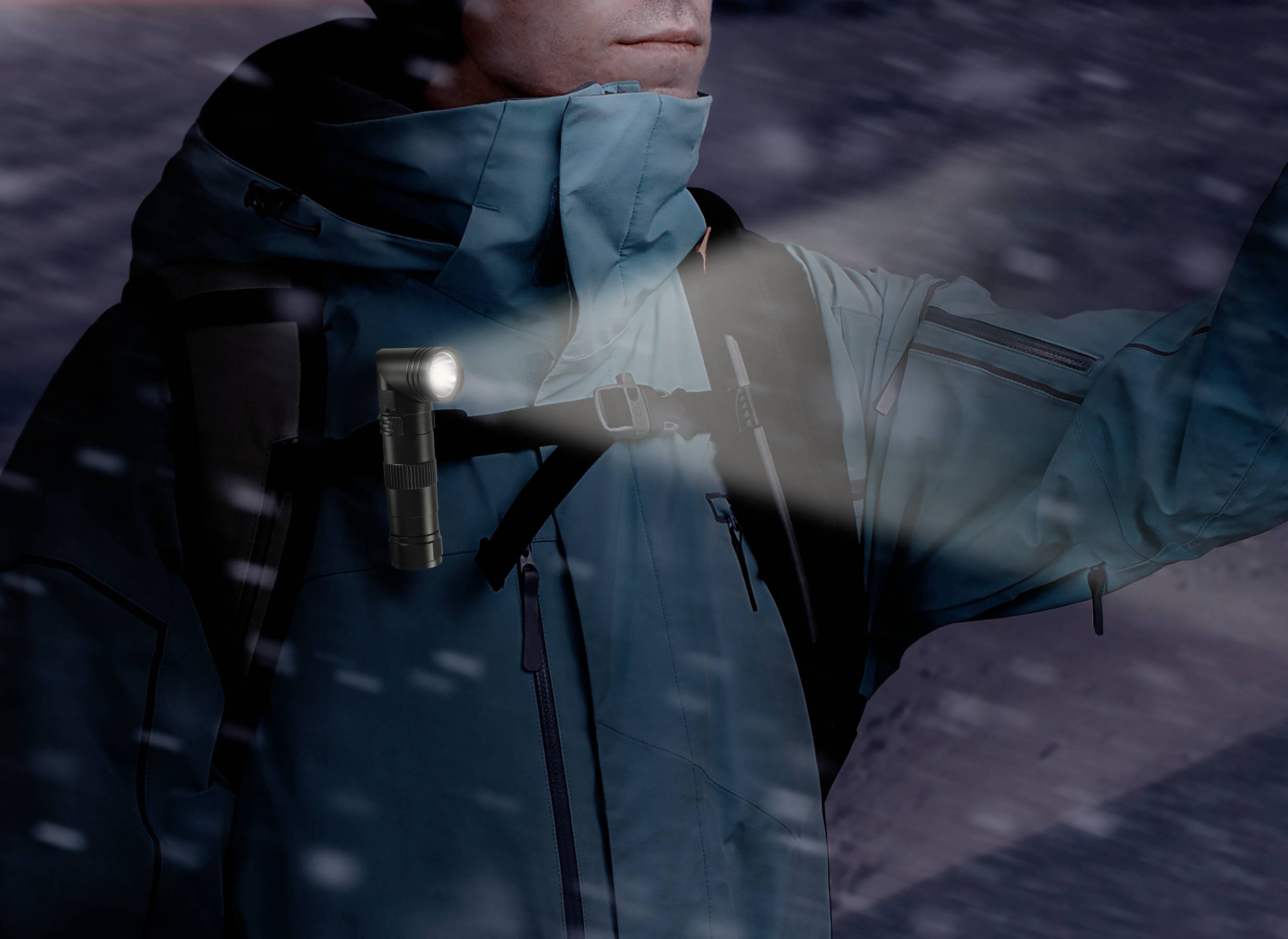Eine Person in Winterkleidung trägt eine Taschenlampe an der Schulter, die im Schnee leuchtet.