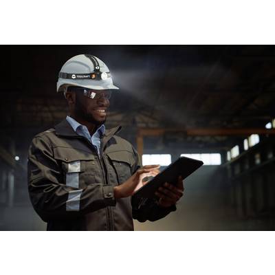 Eine Person in Arbeitskleidung und Helm nutzt ein Tablet in einer Industrieumgebung, möglicherweise zur Inspektion oder Datenaufnahme.