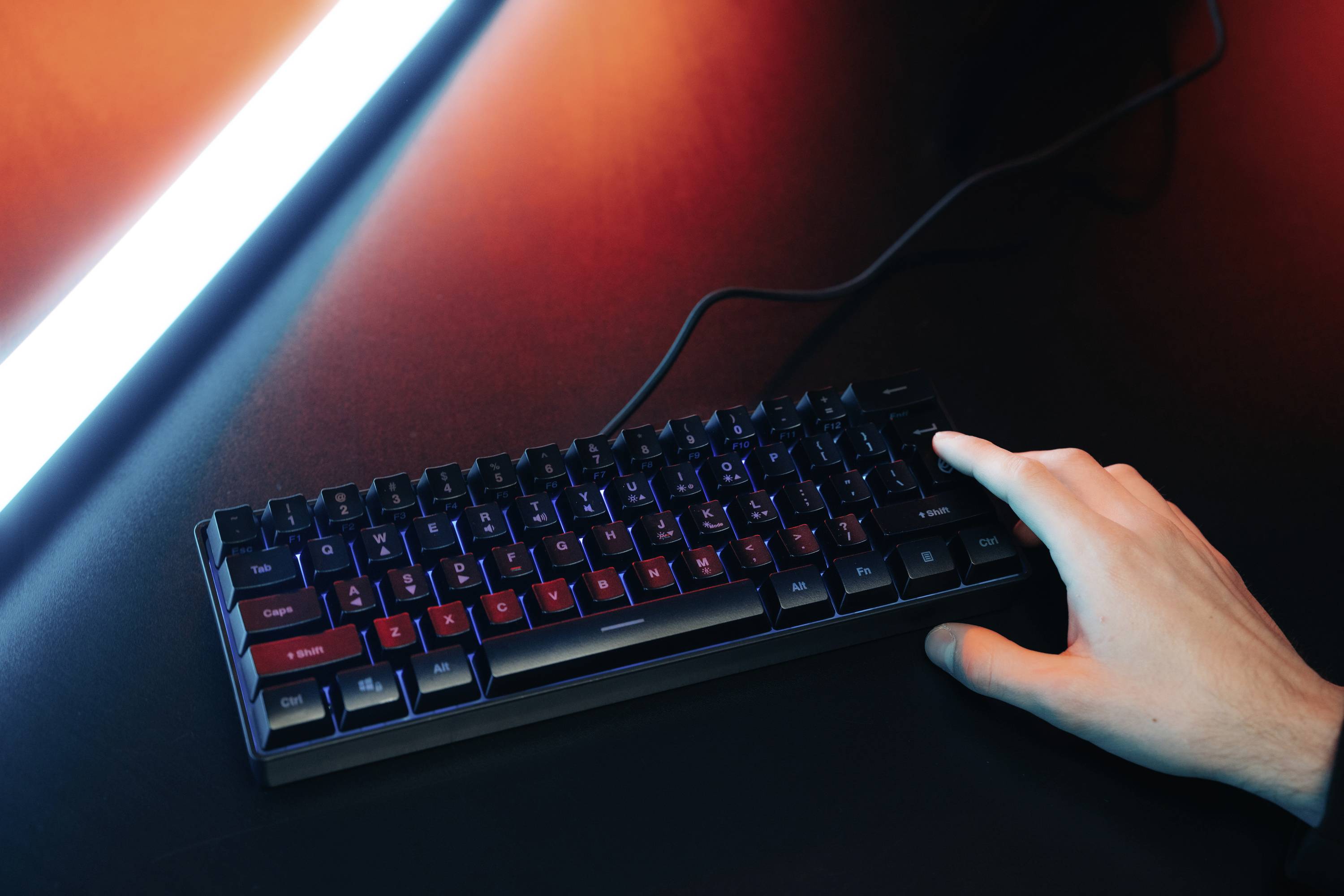 Eine Hand tippt auf eine beleuchtete mechanische Tastatur unter einem roten und blauen Licht.
