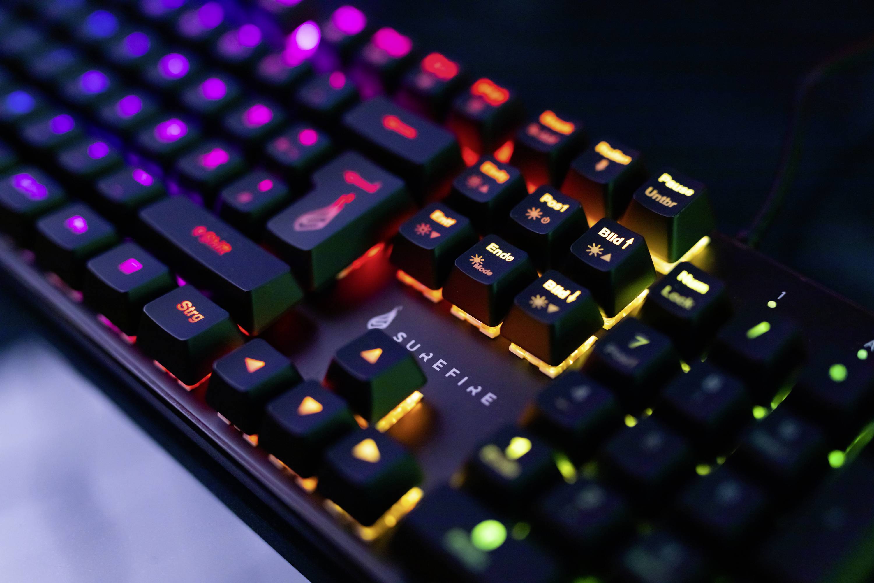 Eine beleuchtete mechanische Tastatur mit bunten RGB-Lichtern in verschiedenen Farben, fokussiert auf die Tasten und das SureFire-Logo.