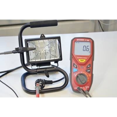 Ein rotes Multimeter zeigt '0,6' an und ist mit einem schwarzen Arbeitslichtgerät verbunden, das auf einem Tisch steht.