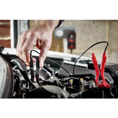 Eine Hand schließt ein schwarzes Überbrückungskabel an die Batterie eines Autos an. Rechts im Bild ist ein rotes Kabel angeschlossen.