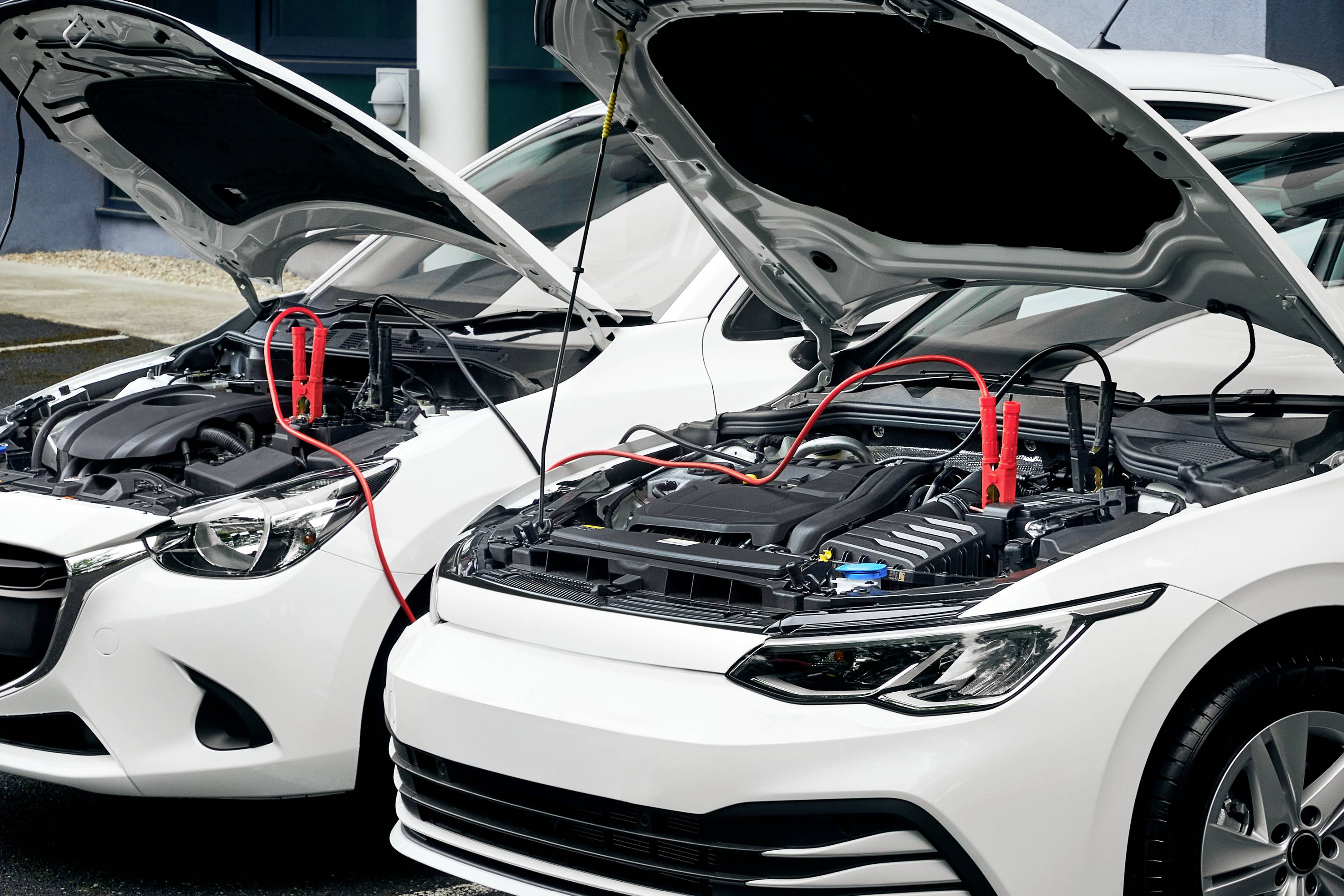 Zwei Autos mit geöffneten Motorhauben, verbunden durch ein Starthilfekabel, was eine Batterieunterstützung symbolisiert.