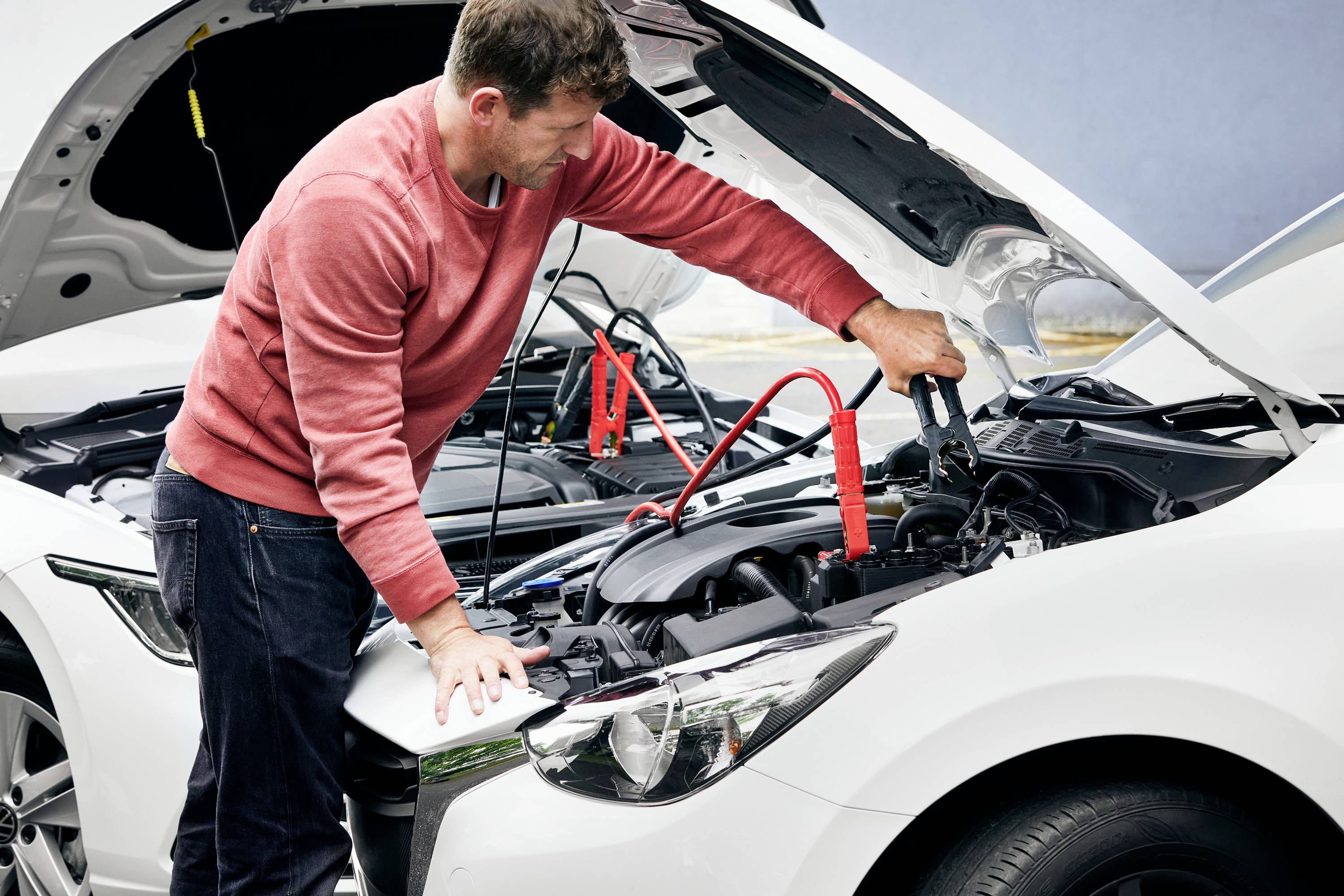 Ein Mann springt ein Auto mit Überbrückungskabeln an. Erneut aufladende Fahrzeugbatterie in Wohngebiet.